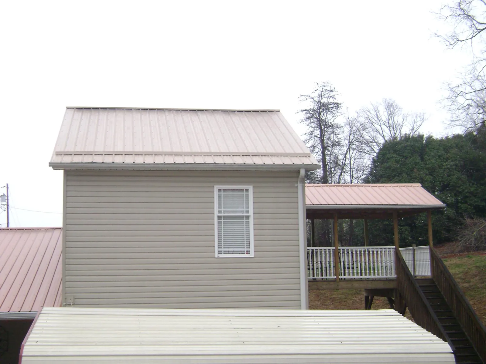 Tan metal roofs on a two story addition and attached porch, from a Roof Replacement job in Pleasant Hill